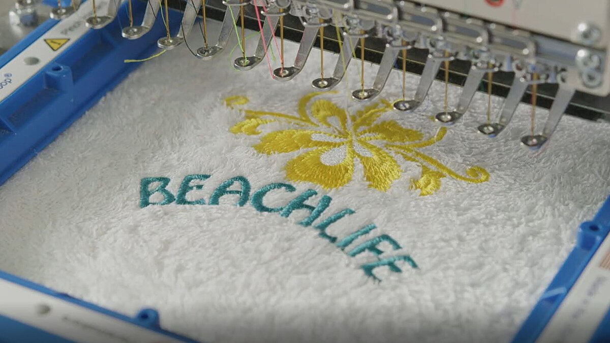 [Translate to Hongkong (Englisch):] Terrycloth towel with a yellow flower and the word Beachlife on an embroidery machine
